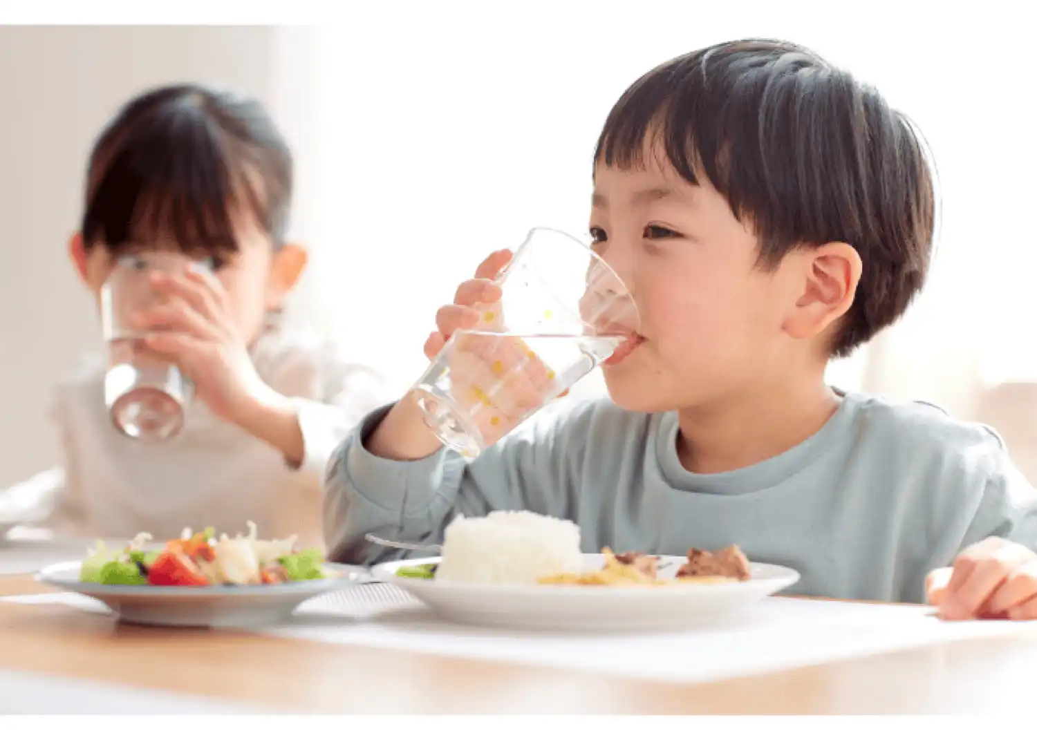 食卓で子どもがグラスの水を飲む様子